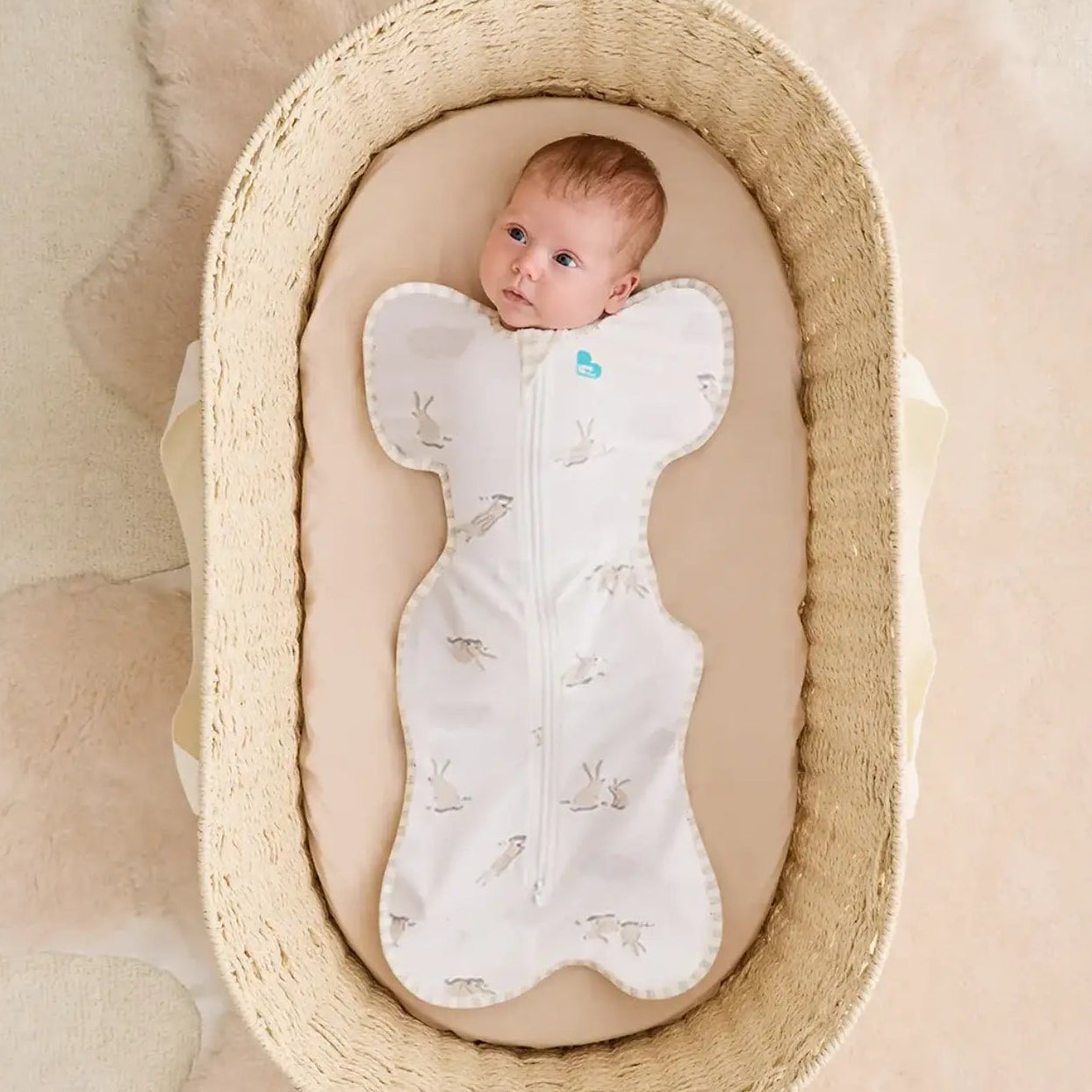 Baby in a wicker basket with a white swaddle blanket on a beige background